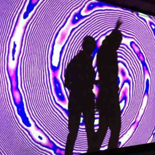 Two standing audience members casting a dancing shadow within an art projection at Pop Up Art Galerie in Hamburg