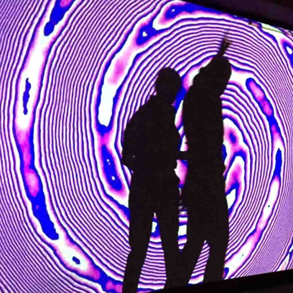 Two standing audience members casting a dancing shadow within an art projection at Pop Up Art Galerie in Hamburg